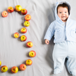 A young baby with the number three spelled out in apples