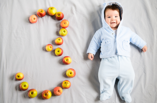 A young baby with the number three spelled out in apples