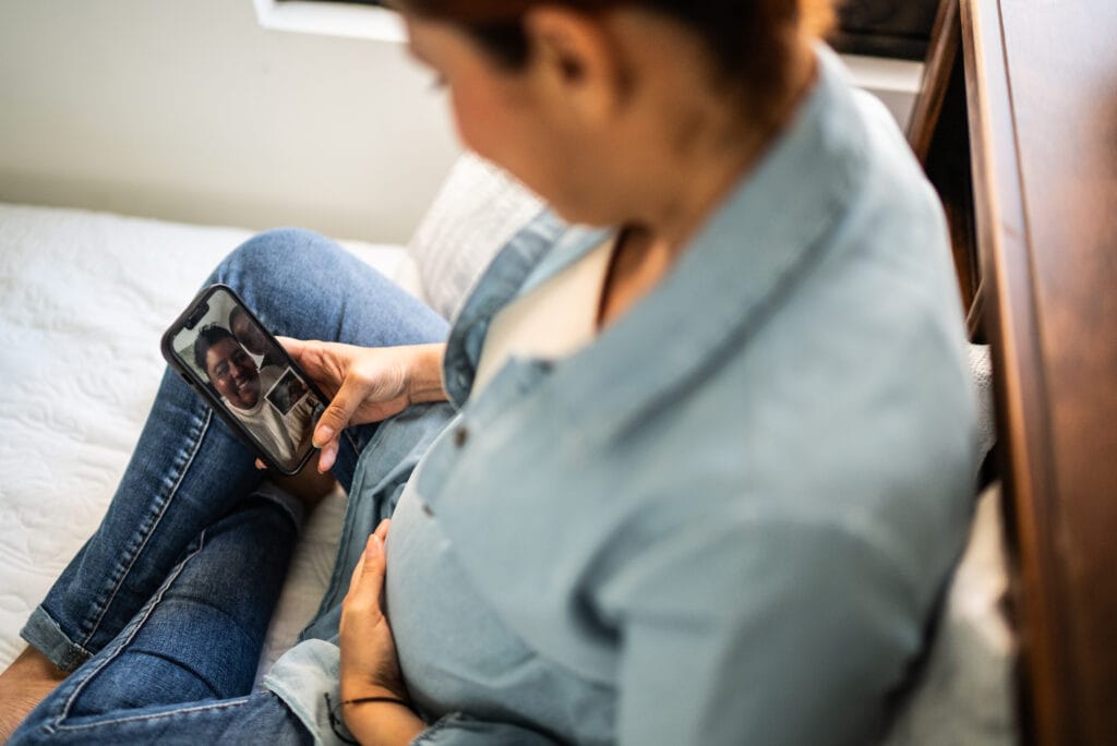 mid adult pregnant talking with friends on video call at home